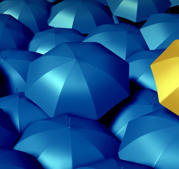 Individual thinking business symbol with a large group of blue umbrellas and standing out from the crowd as a confident yellow umbrella as icons of protection and financial security.